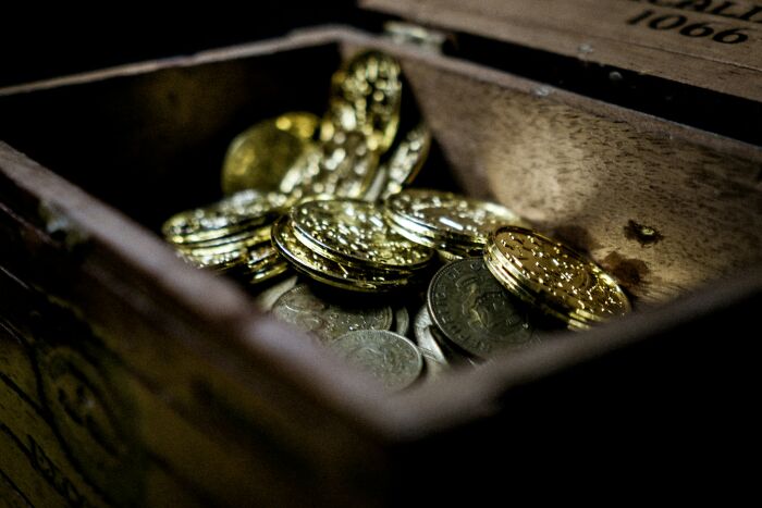 Wooden chest filled with old gold and silver coins representing historical artifacts linked to false history facts.