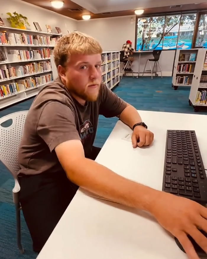 White man sitting at library desk with computer, appearing uneasy in viral video involving racial slur confrontation.