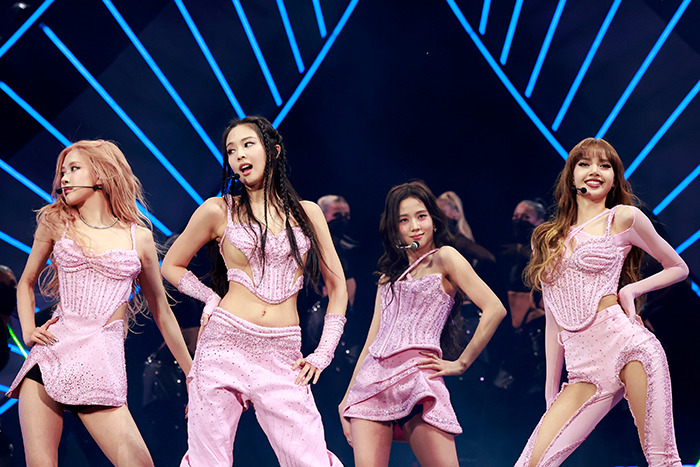 Blackpink's Lisa wearing a risqué pink outfit, dancing on stage with band members and kids visible in the audience. Blackpink's Lisa wearing a risqué pink outfit, dancing on stage with band members and kids visible in the audience.
