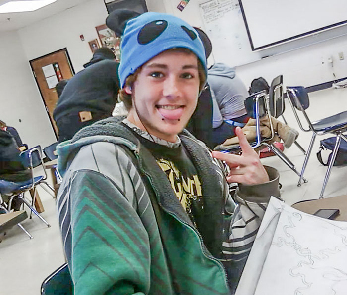 Teen boy wearing a blue cartoon hat in a classroom, smiling and making a gesture, related to cold case breakthrough.