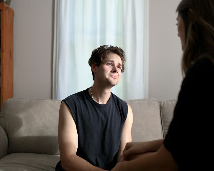Young man in a happy marriage sitting on a couch, sharing relationship tips while holding hands with partner.