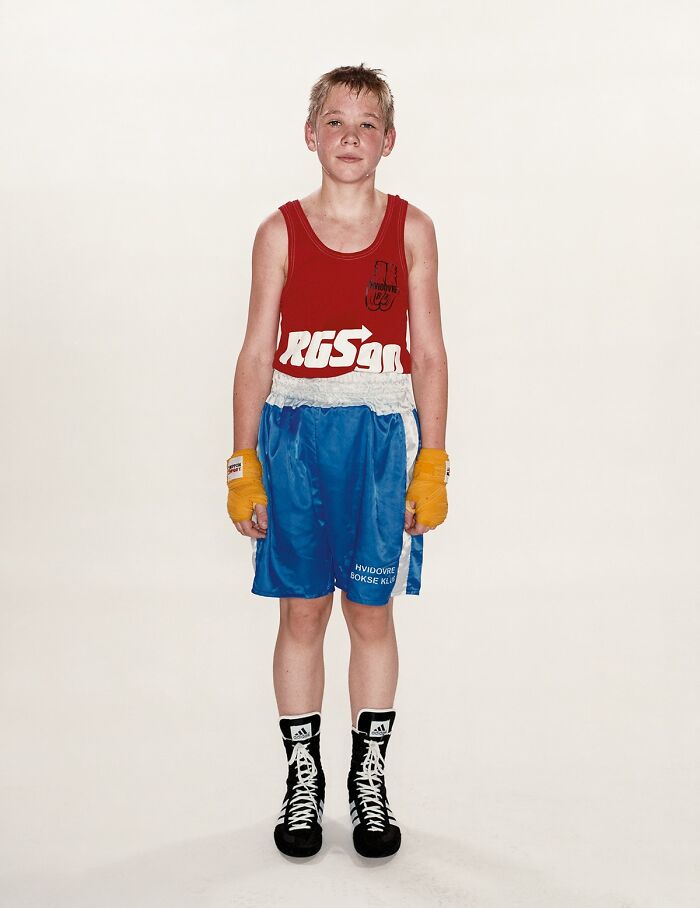 Young boxer wearing red tank top and blue shorts standing before his first match in powerful photographs series.