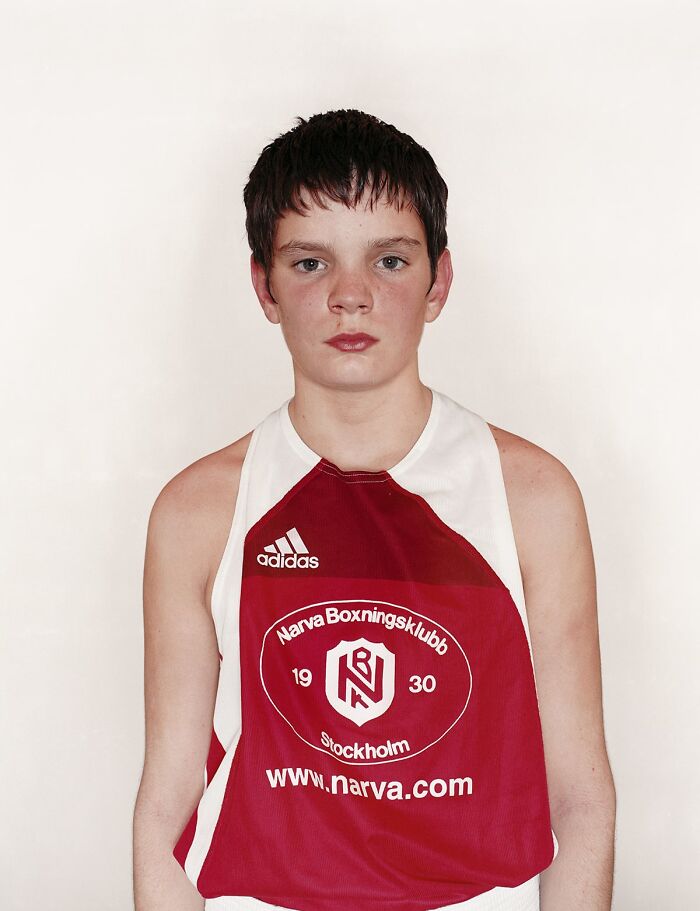 Young boxer wearing red and white gear, standing against a plain background before his first boxing match.