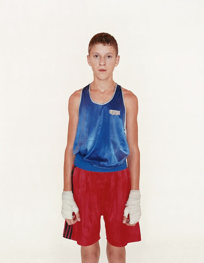 Young boxer wearing blue tank top and red shorts, posing for powerful photographs before their first match.
