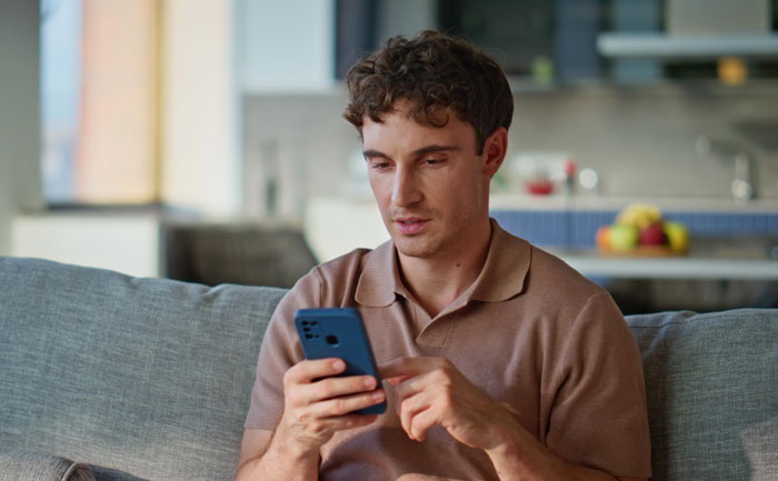 Young man sitting on a couch, looking at his phone with concern, related to boyfriend died friend started messaging topic.