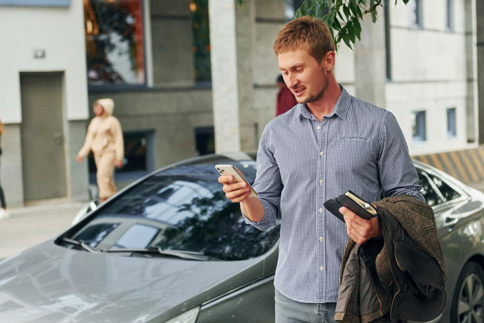 Young man smiling while messaging on his phone outdoors near a parked car, reflecting boyfriend died friend started messaging theme.