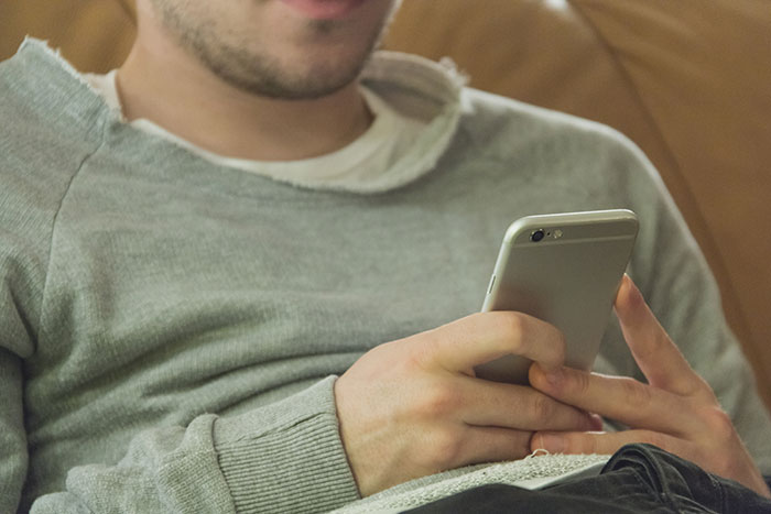 Man in casual grey sweater holding a smartphone, representing a hidden device found in closet prank by boyfriend.