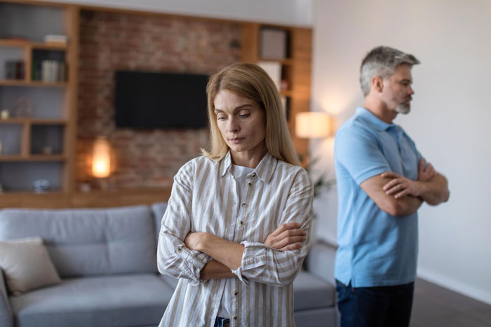 Woman and boyfriend standing apart in living room, tense and upset over survivor benefits and relationship issues.