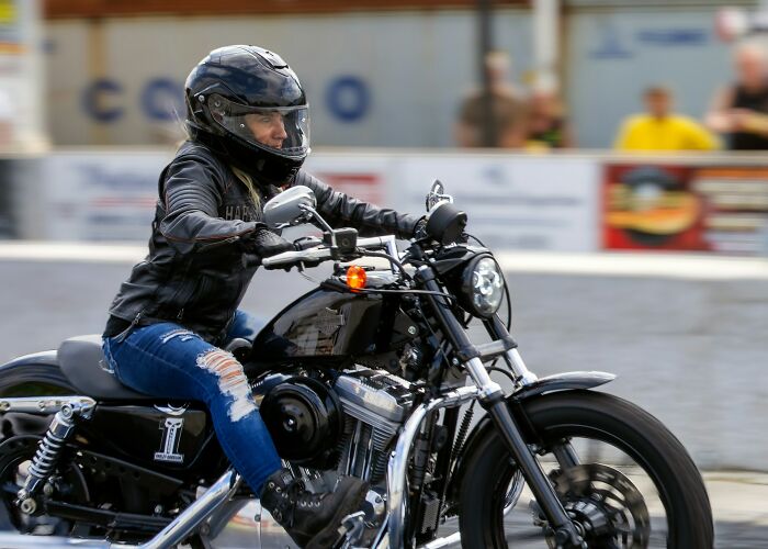 Woman in a black helmet and leather jacket riding a motorcycle, showcasing real life moments more interesting and bizarre than fiction.