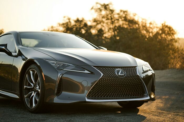 Sleek black Lexus sports car parked on a dirt road at sunset, highlighting luxury and stylish design details.