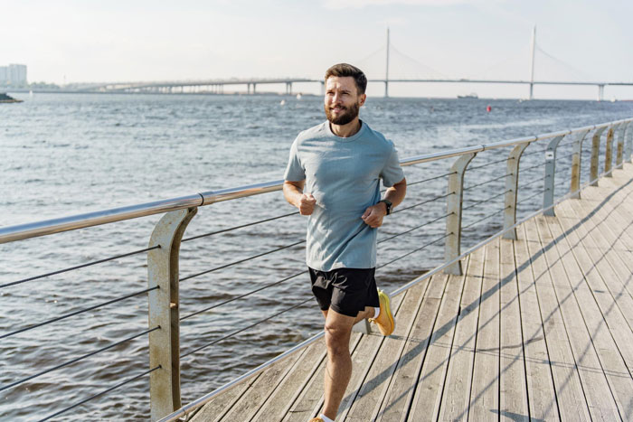 Man running along waterfront on boardwalk, representing dad preparing for marathons while mom faces heavy periods and anemia.