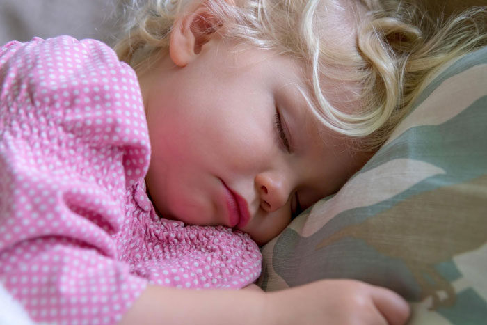 Sleeping toddler girl with blonde hair resting on pillow, representing mom caring for child amid anemia and hair fall challenges.