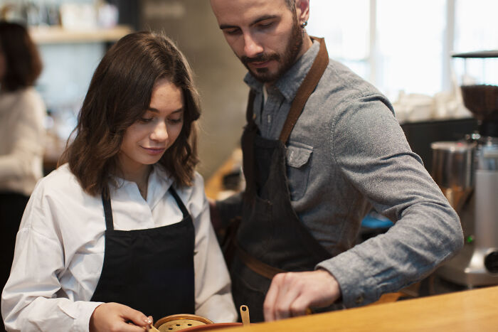 Two baristas in aprons focus on preparing coffee in a cozy café, illustrating out-of-touch moments in customer service.