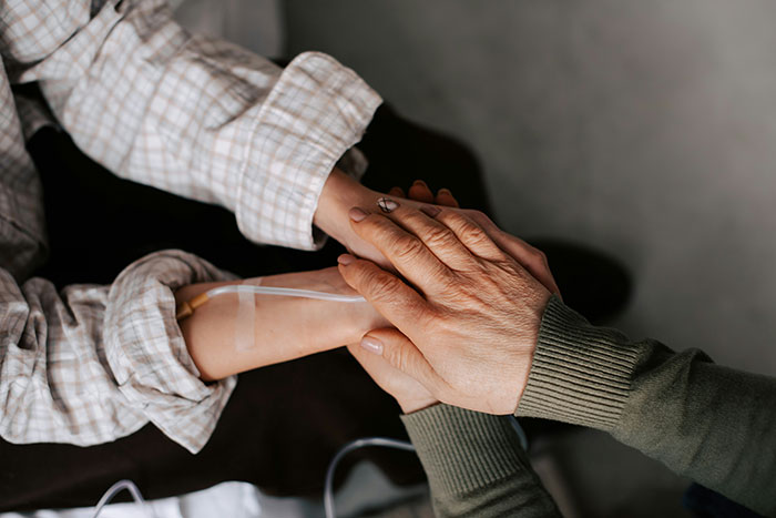 Two people holding hands, one with an IV line, symbolizing support during a cancer rumor affecting J.K. Rowling's team. Two people holding hands, one with an IV line, symbolizing support during a cancer rumor affecting J.K. Rowling's team.