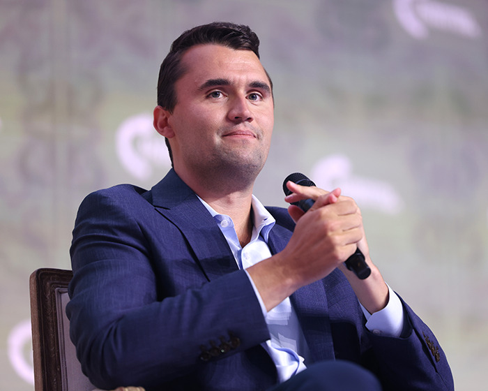 Man in blue suit holding a microphone, representing Tyler Robinson in a discussion about Kirk crime theories.