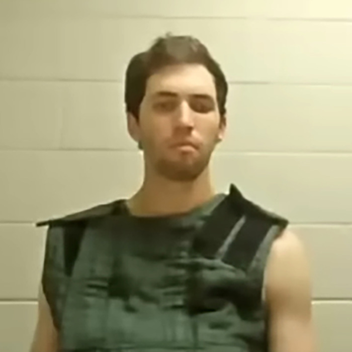 Young man wearing a protective vest in a holding cell, related to Candace Owens and Tyler Robinson claims.