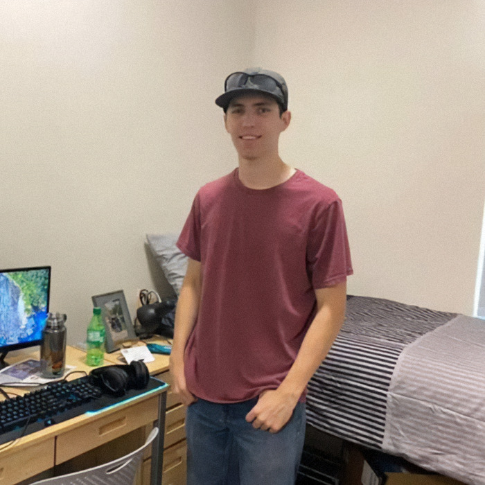 Young man standing in a casual room setting with computer gear and bed, related to Tyler Robinson exclusive photo claim.
