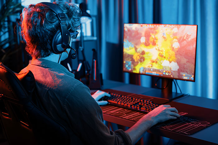 Person wearing headset playing a video game on a desktop computer, illustrating themes of catfish stories and online interactions.