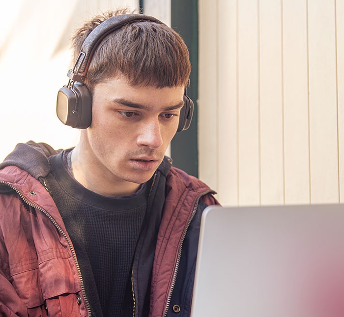 Young man wearing headphones, looking intently at laptop screen, reflecting on catfish stories and online DMs.