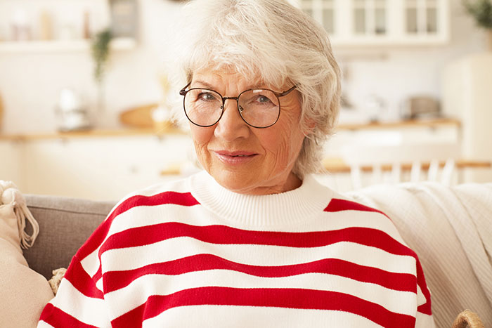 Elderly woman in glasses and striped sweater, reflecting on catfish stories and trusting online DMs with caution.
