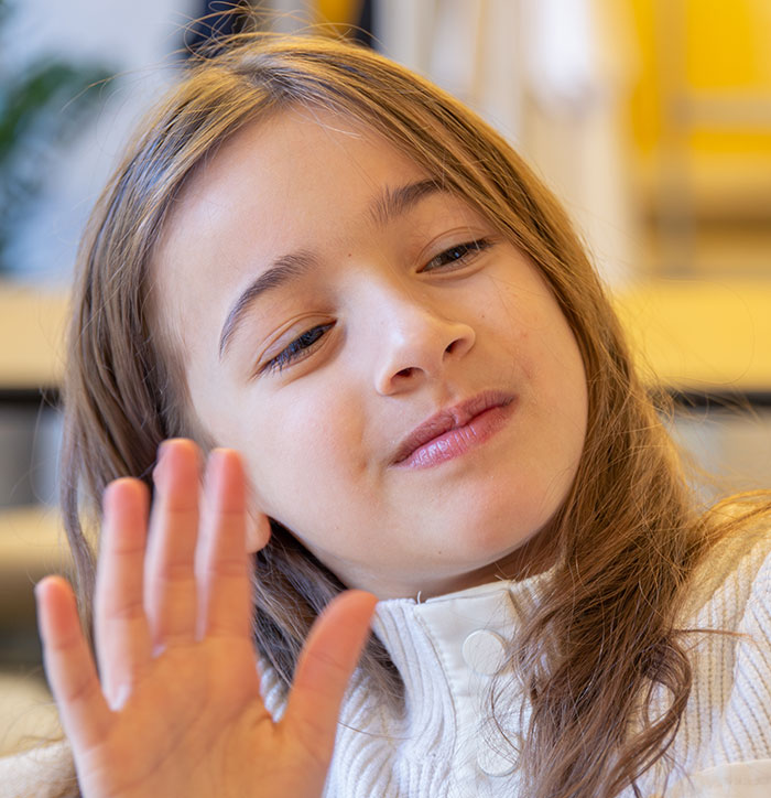 Young girl raising her hand with a thoughtful expression, illustrating feelings related to catfish stories and online trust.