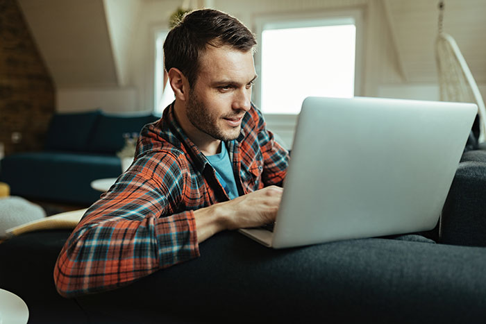 Man using laptop at home, reflecting on catfish stories and unsure about the messages he has received.
