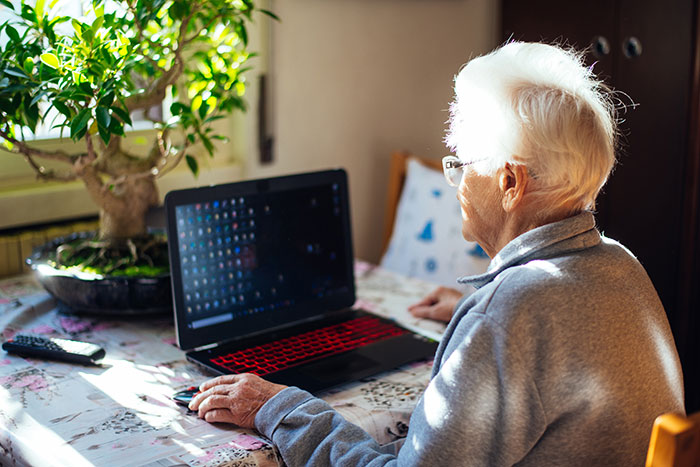 Elderly person using a laptop at home, reflecting on catfish stories and questioning online direct messages.