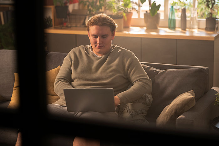 Young man sitting on a sofa using a laptop, reflecting on catfish stories and questionable direct messages.