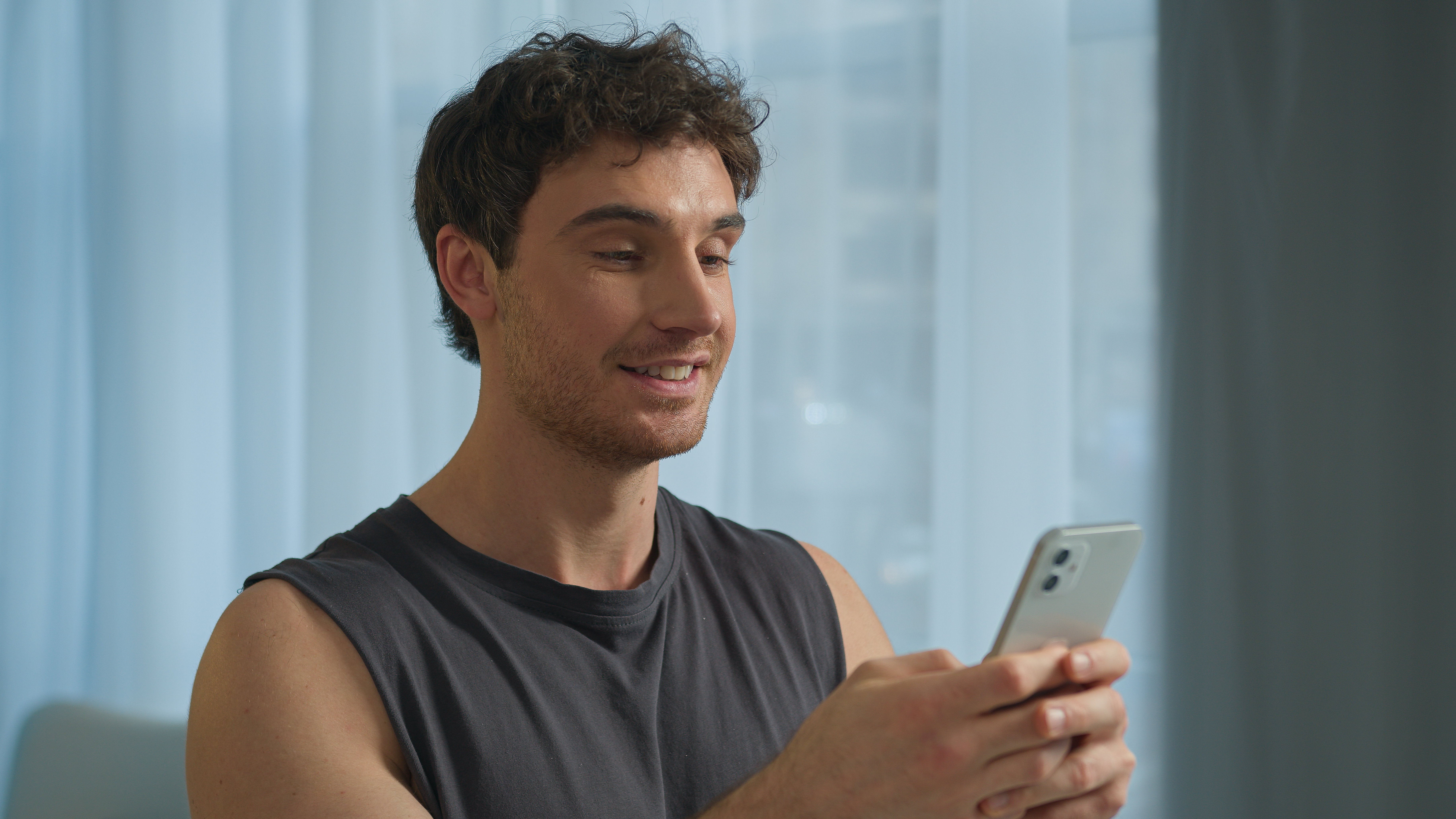 Young man using smartphone smiling, illustrating use of Russian bots to impact bank social media after funds restriction.