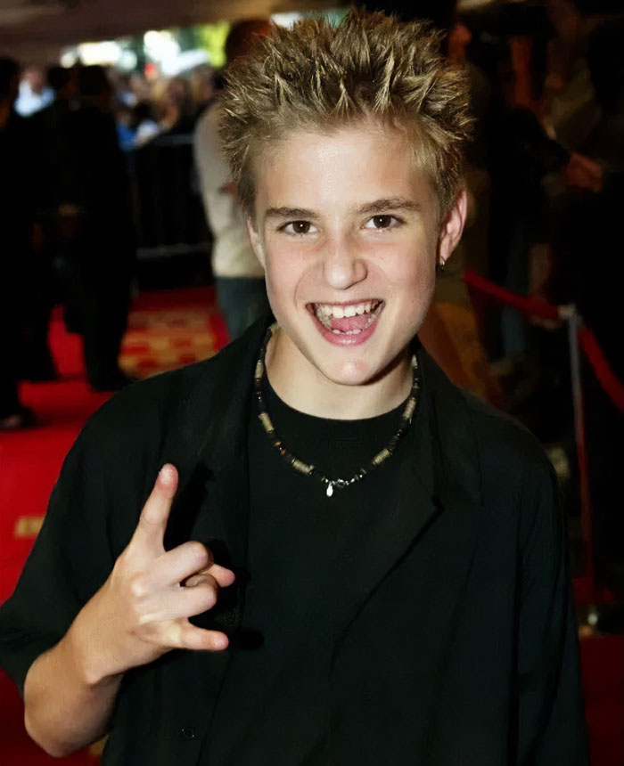 Young child star with spiked hair smiling and making a hand gesture at an event red carpet, representing child stars who passed away.