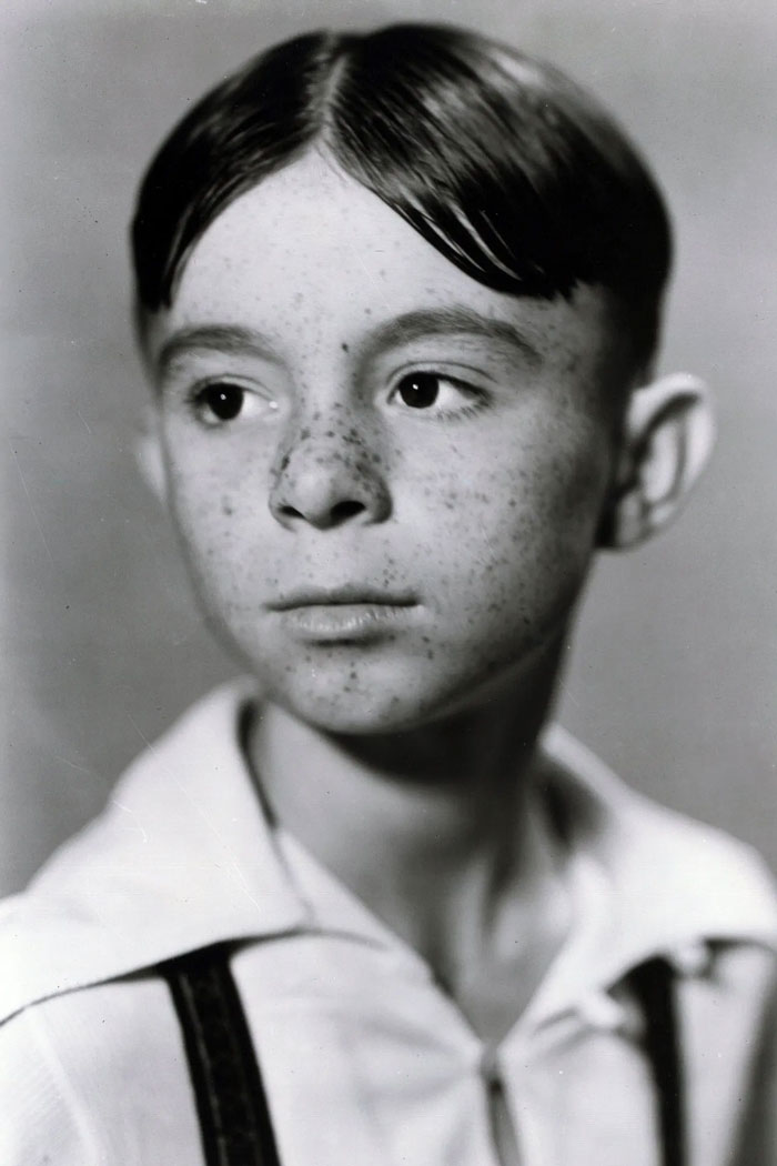 Black and white portrait of a young boy with freckles and a somber expression, representing child stars who passed away young.