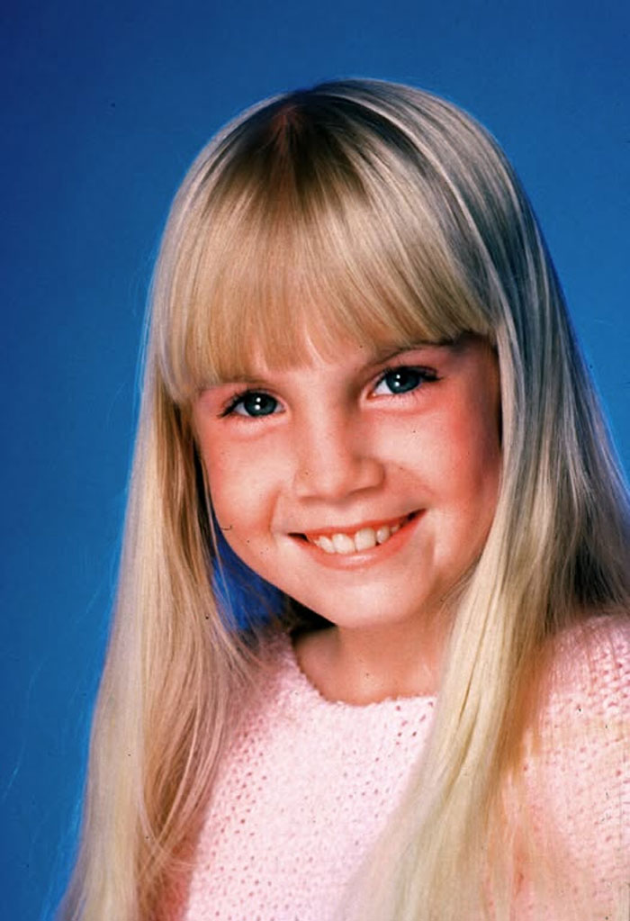 Smiling young blonde child star with blue eyes wearing a pink sweater, representing child stars who passed away young.