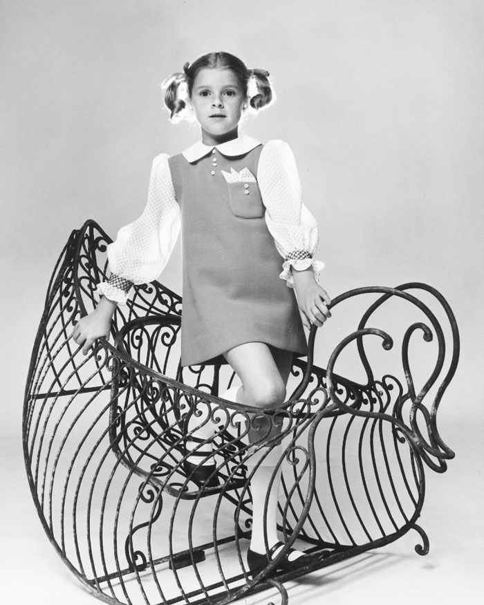 Young child star posing in a vintage dress on an ornate metal rocking horse, representing child stars who passed away young.