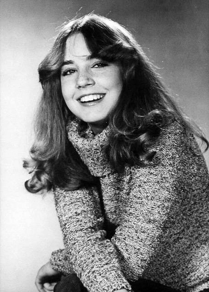 Black and white portrait of a smiling young female child star in a knit sweater, representing child stars who passed away young.