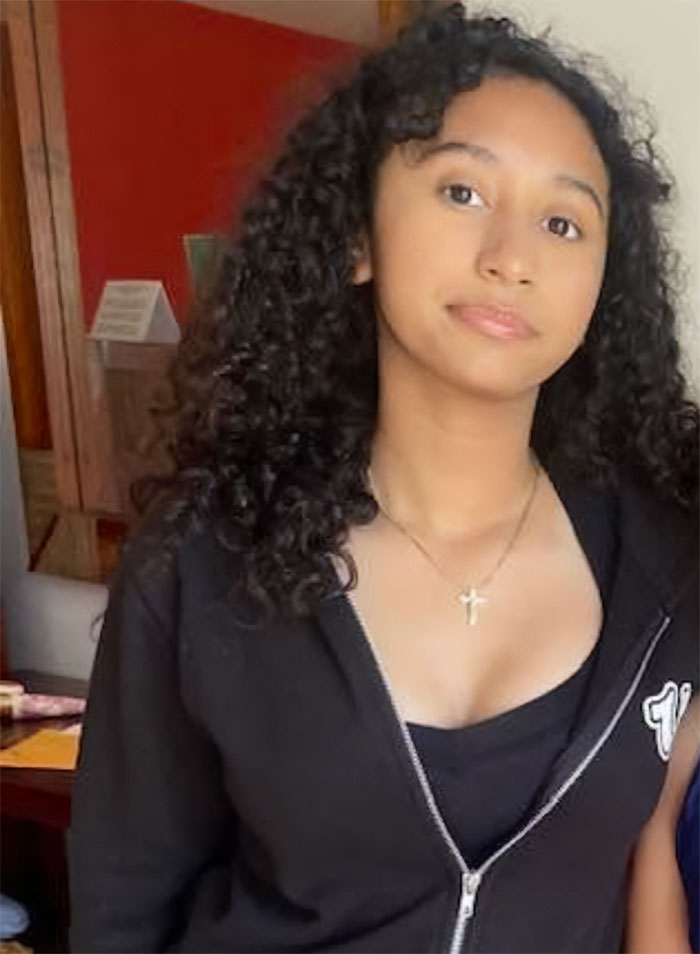 Teen girl with curly hair wearing a black zip-up hoodie and cross necklace at home, related to missing girl found in singer D4vd&rsquo;s Tesla case.