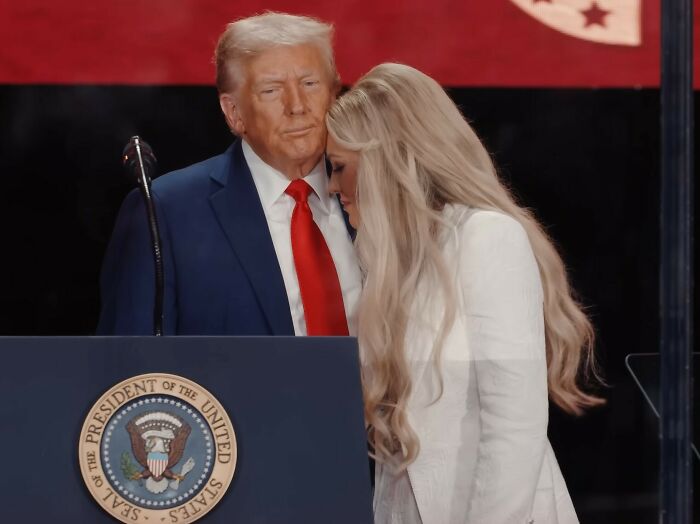 Man in blue suit and red tie standing with woman in white dress near podium with presidential seal during heated debate.