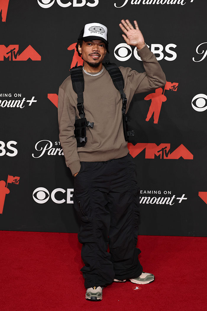 Young man in casual streetwear waving on the red carpet at the 2025 Video Music Awards worst dressed stars event.