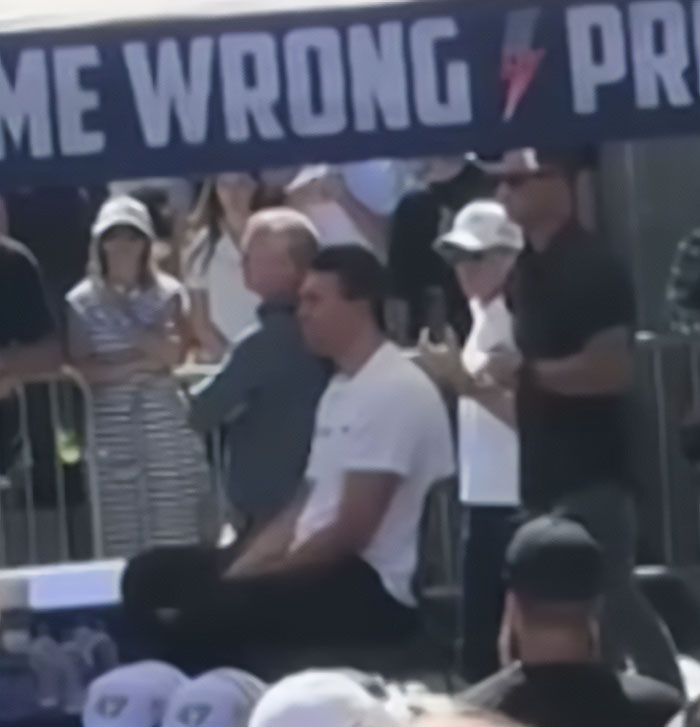 Crowd gathered near a barricade with a visible protest sign, relating to new CCTV footage of the main suspect's escape.