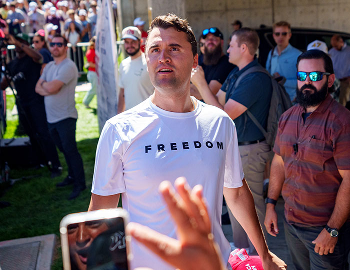 Man wearing a white freedom shirt at an outdoor event with a crowd, related to Iryna Zarutska and Charlie Kirk.