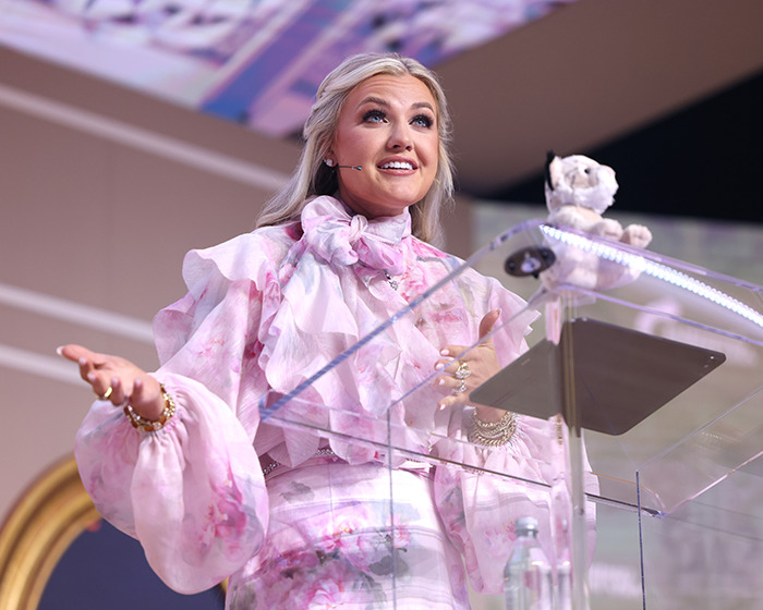 Erika Kirk speaking at a podium, wearing a pink floral outfit, after being appointed CEO of Turning Point USA.