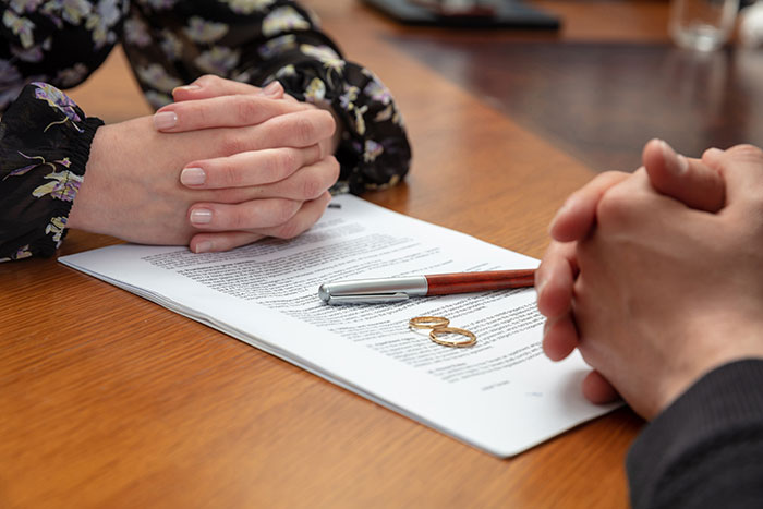Couple with wedding rings and documents on table, symbolizing husband outsmarting cheating wife in divorce settlement.