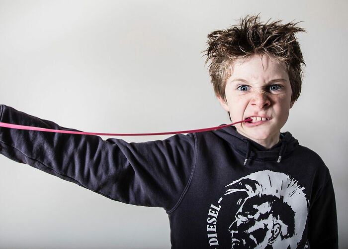 Boy with wild hair pulling gum with his teeth, expressing frustration and defiance related to wildest rules people grew up with.