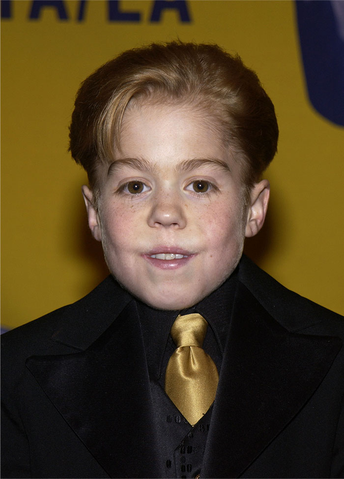 Young male child star dressed in black suit and gold tie at an event, representing child stars who passed away young.