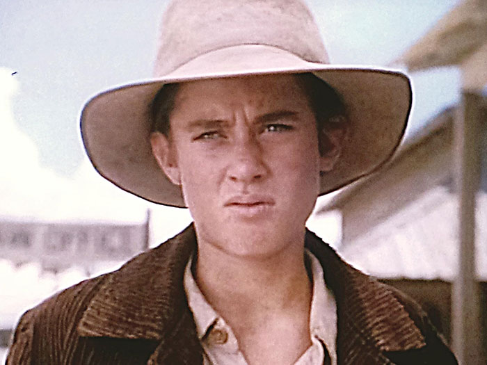 Young male child star wearing a wide-brimmed hat and brown jacket in a vintage outdoor setting, representing child stars who passed away.
