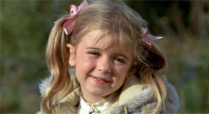 Young blonde child star smiling outdoors with pink hair ribbons, representing child stars who passed away tragically young.