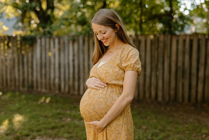 Pregnant mother smiling and gently holding her belly outdoors in a yellow dress, expecting her child soon. Pregnant mother smiling and gently holding her belly outdoors in a yellow dress, expecting her child soon.