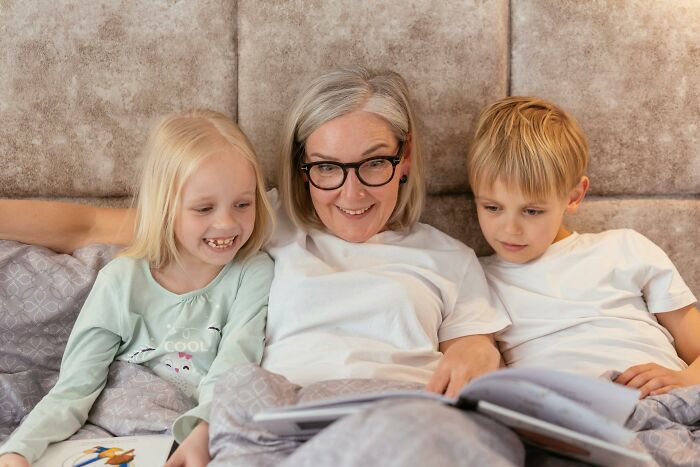 Pregnant mother with two children smiling and reading a book together on a cozy bed at home. Pregnant mother with two children smiling and reading a book together on a cozy bed at home.