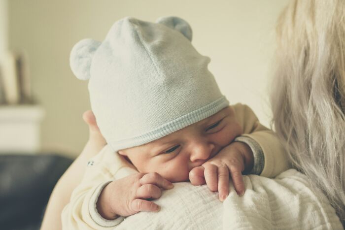 Newborn baby wearing a soft hat resting on adult's shoulder, symbolizing unexpected events causing loss of savings.