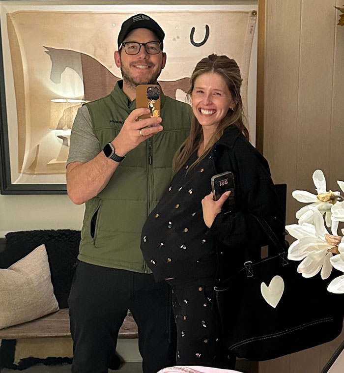 Chris Pratt smiling with a pregnant woman, casual indoor selfie, highlighting viral clip of his unique praying style.