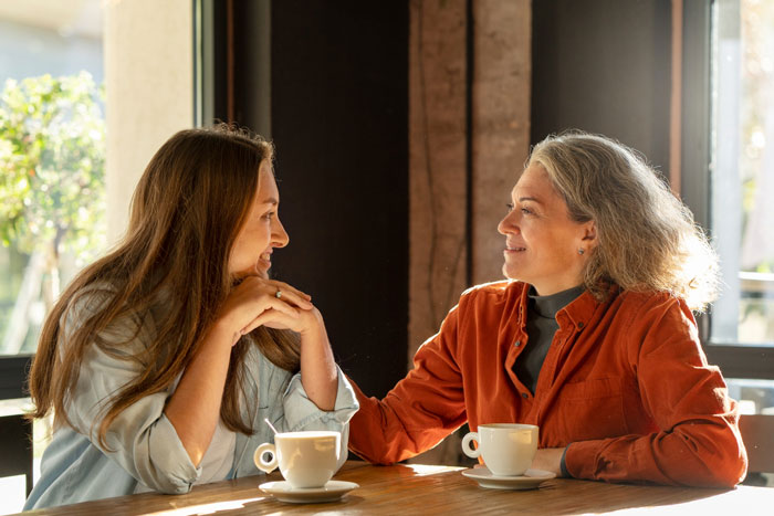 Two women having coffee in a sunlit cafe, sharing a warm moment related to Christian rapture and money dollars concepts.